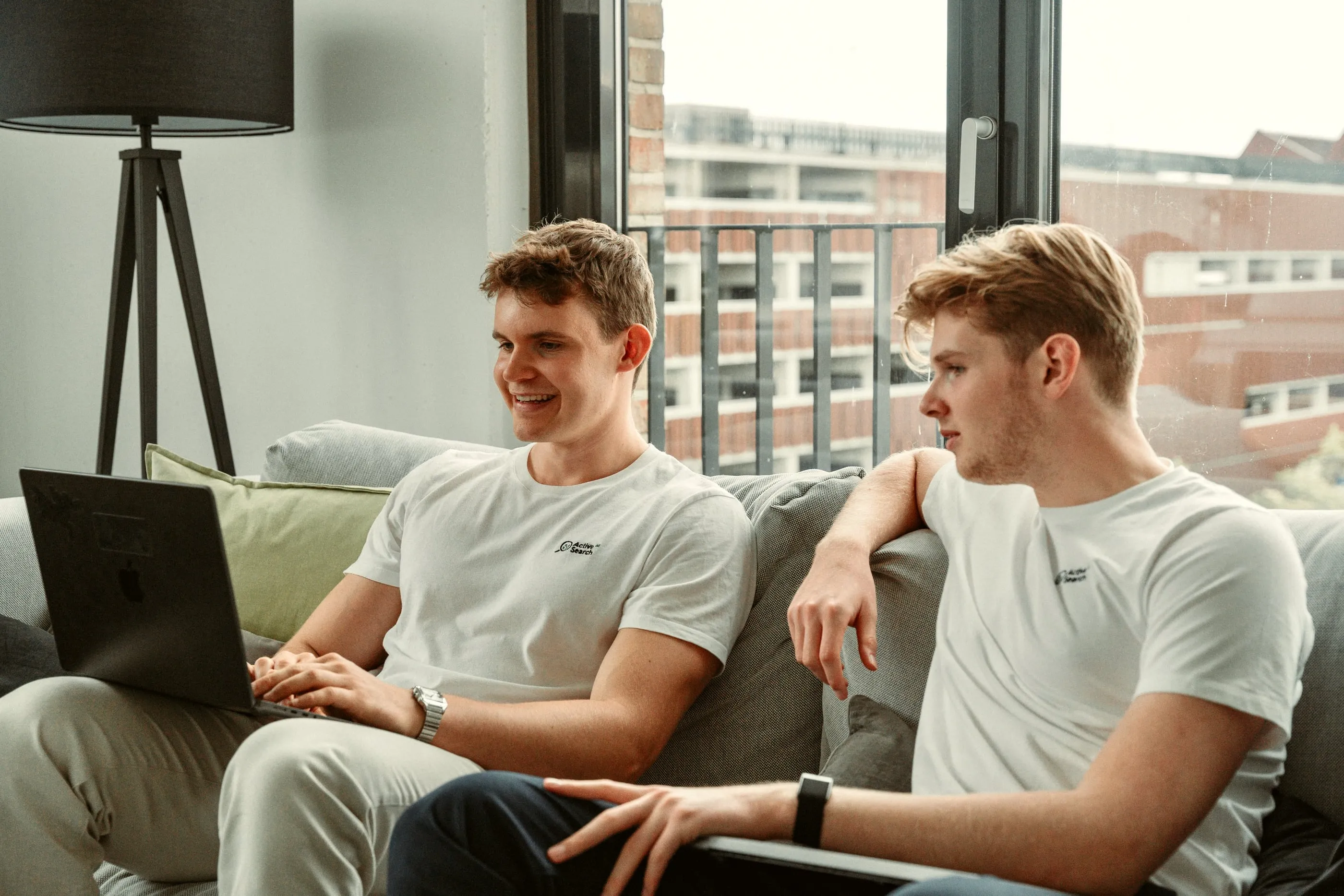 Zwei Mitglieder des Teams von Active Search mit dem Laptop auf dem Sofa im Büro