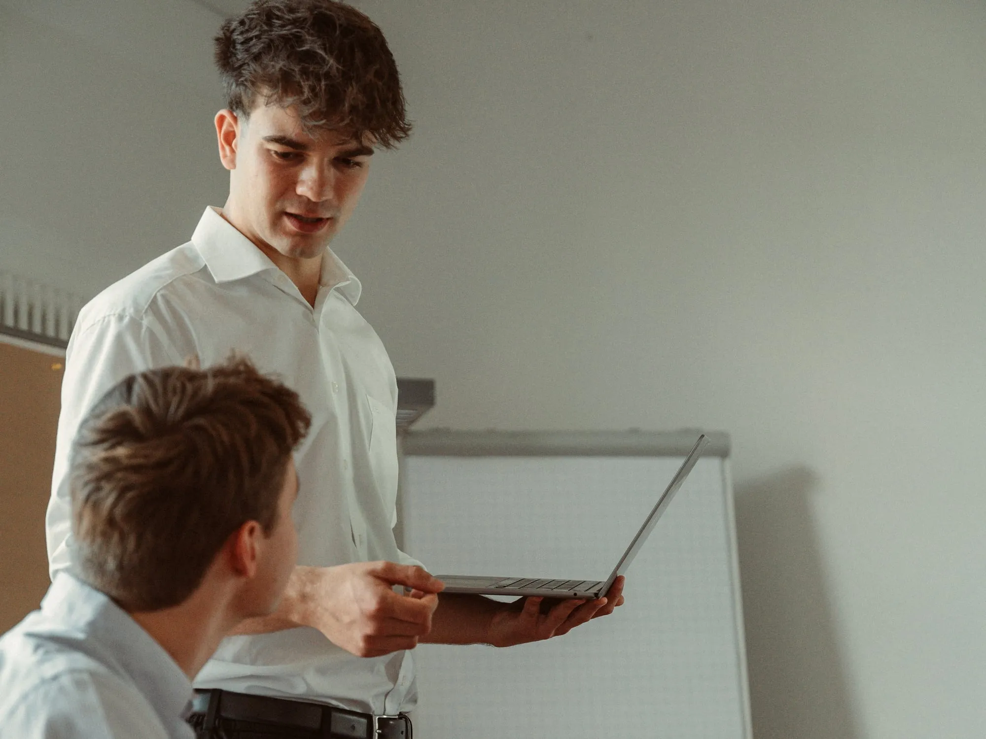 Ein Teammitglied zeigt einem anderen etwas auf dem Laptop, dahinter ein Flipchart
