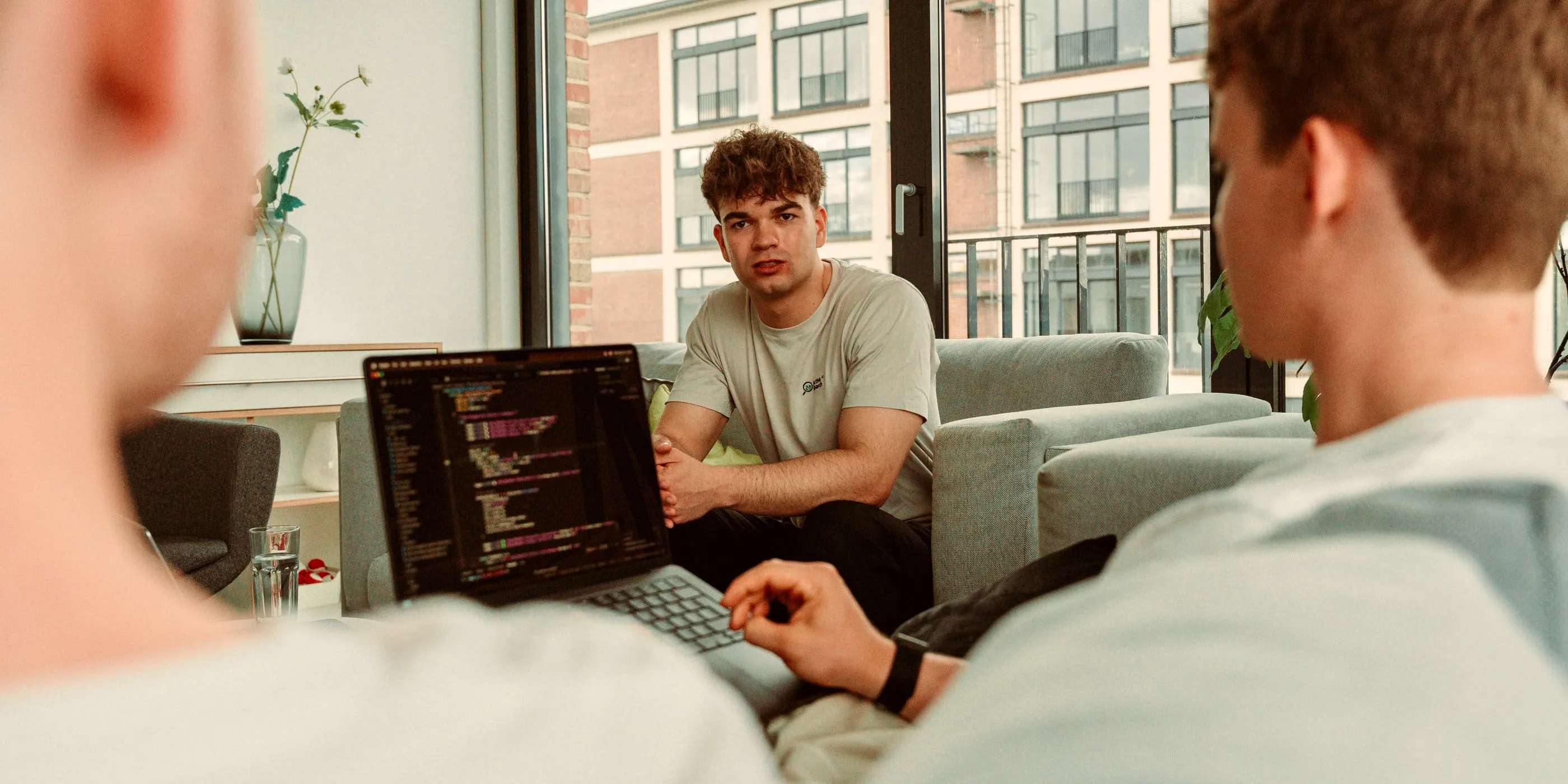 Zwei Teammitglieder im Gespräch auf dem Sofa, im Vordergrund ein Laptop mit Code