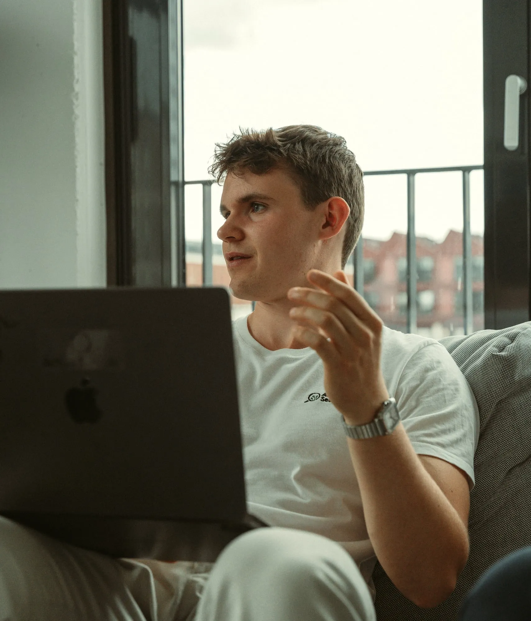 Ein Teammitglied auf dem Sofa am Fenster, den Laptop auf dem Schoß, erklärt etwas im Gespräch
